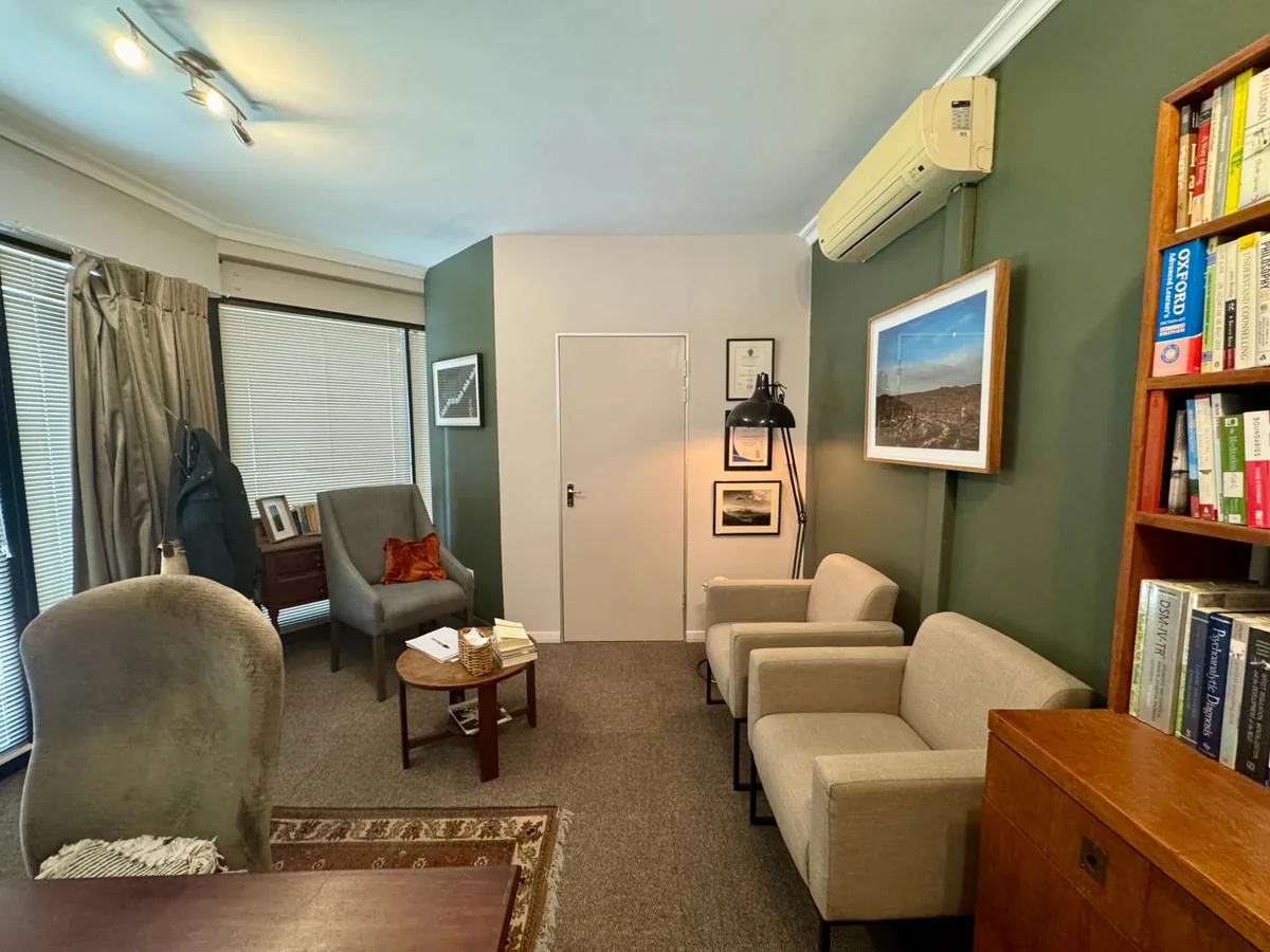 The counselling room: a grey armchair by the window, a floor lamp, and two cream armchairs against a green wall beside a bookshelf